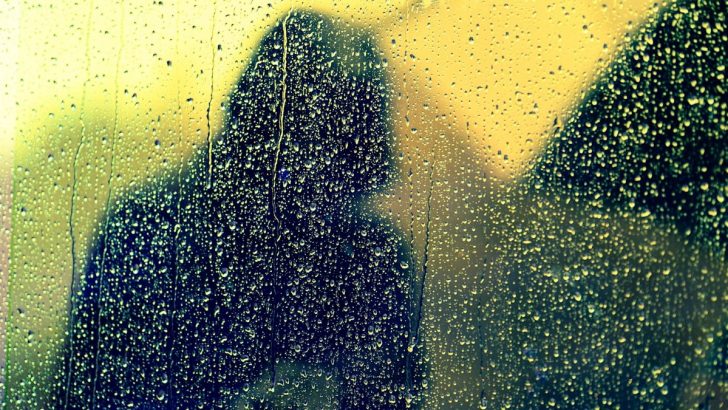 Hooded figure reflected in rainy glass